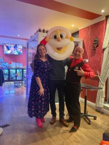 A man wearing a santa balloon helmet with two people standing beside him. 